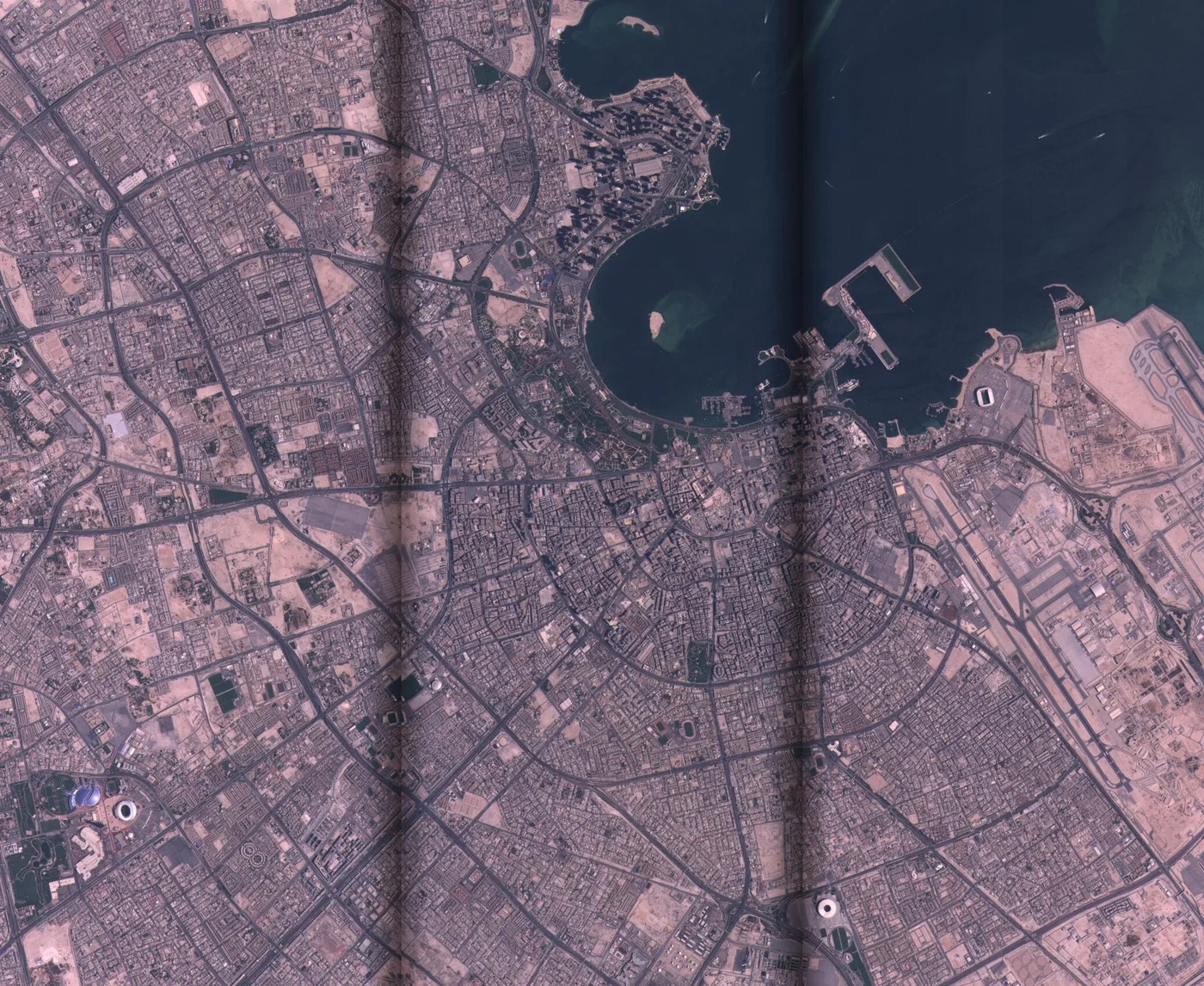 Satellite image of Doha, Qatar, showing the Corniche bay, the city grid, the port, and Hamad International Airport