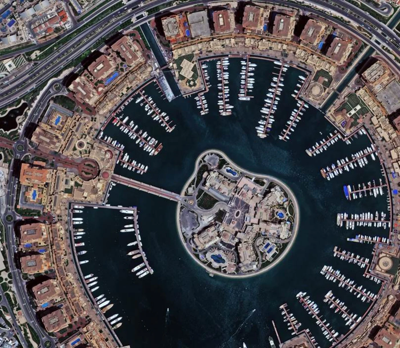 Satellite image of a circular marina district within The Pearl-Qatar, Doha, showing residential buildings and berthed boats