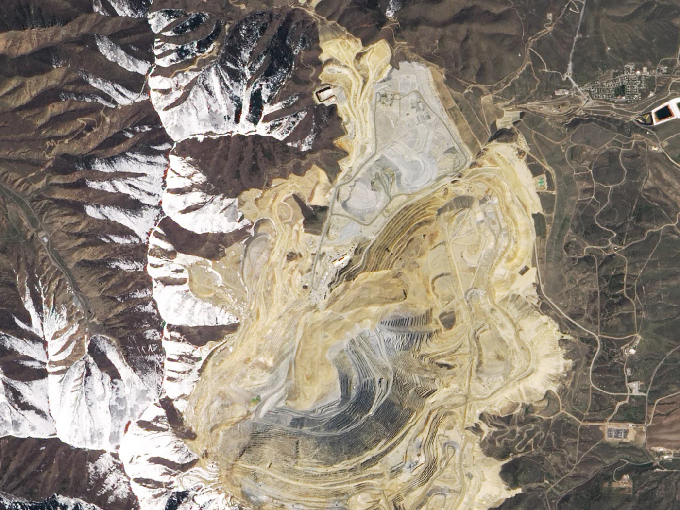 Satellite image of Bingham Canyon copper mine in Utah showing the pale debris fan of the 2013 landslide spread across the lower pit benches against snow-covered mountains