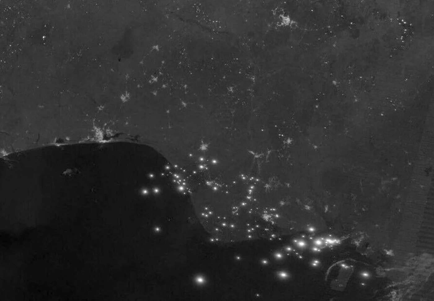 Nighttime VIIRS satellite image of the Niger River Delta, Nigeria, showing bright gas flares from oil and gas infrastructure outshining surrounding city lights