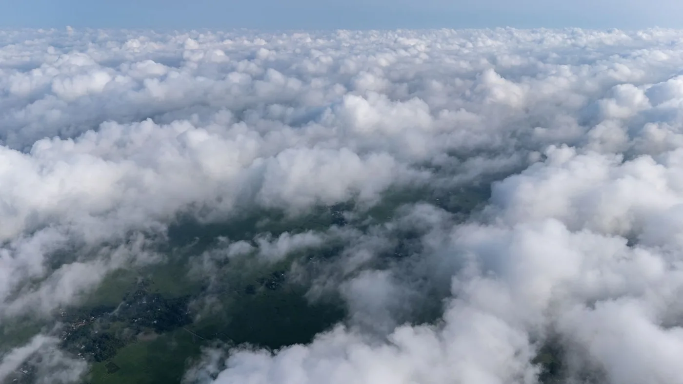 Aerial view through a break in dense cloud cover showing a small clear patch of green landscape below, illustrating how a scene can look mostly clouded while still leaving a usable gap over a specific area
